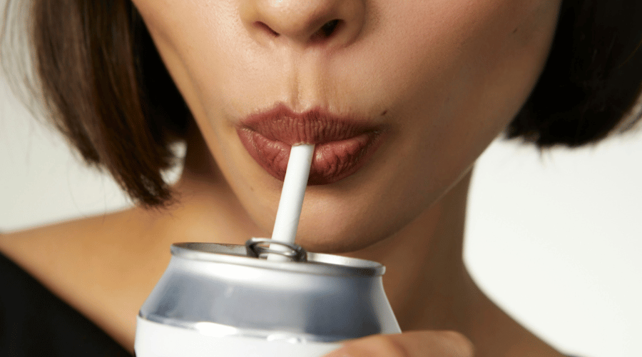 Close-up van een vrouw met korte, donkere haren die uit een frisdrankblikje drinkt met een rietje. Haar volle, goed verzorgde lippen benadrukken het belang van hydratatie en zelfzorg, perfect passend bij het thema van een skin detox.