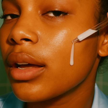 Translation missing: nl.Jonge vrouw met donkere huid brengt het transparante Facile Brighten Pigment Serum aan op haar wang met een pipet voor een egale teint