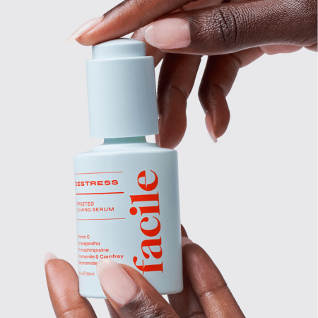 Hand houdt Facile Destress Calming Serum fles vast, toont het minimalistische design met oranje logo en productinformatie.