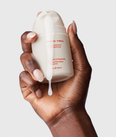Hand houdt Facile Dew You serum vast terwijl een druppel hyaluronzuur van de dispenser valt, wat de vloeibare textuur en eenvoudige dosering toont.