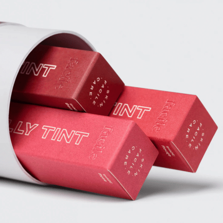 Drie rode Facile Lip Jelly Tint-doosjes die deels uit een witte koker glijden; cadeauklare presentatie van de trio-set.