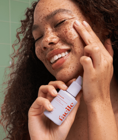 Persoon met stralende huid en sproeten houdt het Facile Skin Clear Acne Serum vast, toonend de verhelderende resultaten van het product.